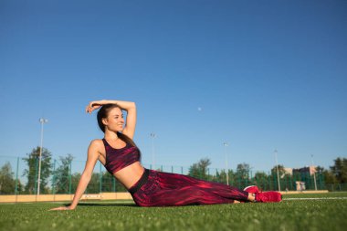 Oturma ve açık havada stadyum alanı alanı üzerinde rahatlatıcı spor giyim mutlu genç sporcumuz. Sağlıklı yaşam konsepti, spor aktivitesi.
