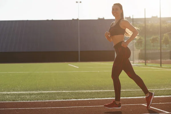 年轻的运动型女子运动员在晚上在体育场跑道上慢跑。健康的生活方式的概念. — 图库照片