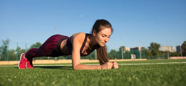 Junge, fröhliche Sportlerin in Sportbekleidung, die draußen auf dem Sportplatz Bretter schlägt. gesunder Lebensstil, sportliche Betätigung. — Stockfoto