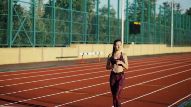 Giovane atleta sportiva che beve acqua sulla pista dello stadio in serata. Stile di vita sano concetto . — Video Stock