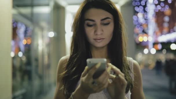 밤 도시의 거리에서 스마트폰 사용 하는 여자. 그녀는 메시지 또는 찾고 뉴스 피드 작성. — 비디오