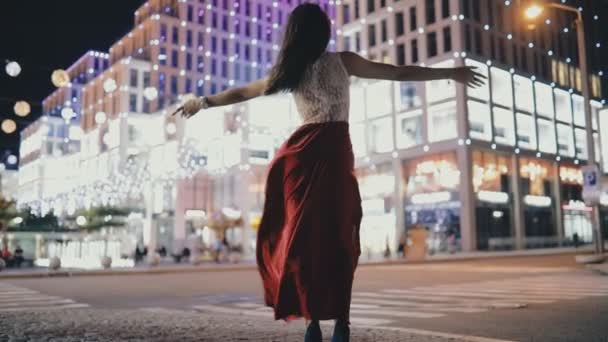 Kusząca Kobieta w czerwonej sukience cieszyć się wolnością i podnieść ręce w nocy miasto ulica — Wideo stockowe