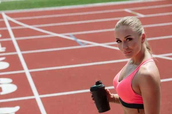 Joven atleta deportista en ropa deportiva de agua potable o cóctel de proteínas de agitar en pista de estadio — Foto de Stock