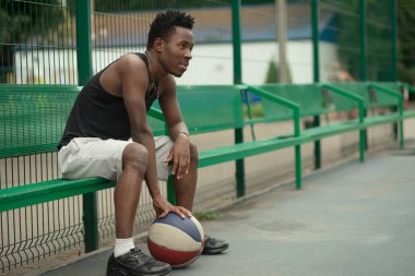 Basketbol sahası üzerinde oturan Afrikalı-Amerikalı adam portresi