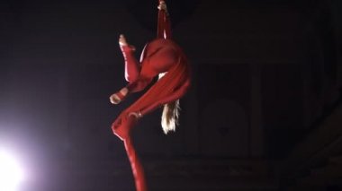 Kadın hava jimnastikçi performans üzerinde kırmızı ipek bir sirk aşamasında döndürün. Heyecan verici akrobatik gösterisi.