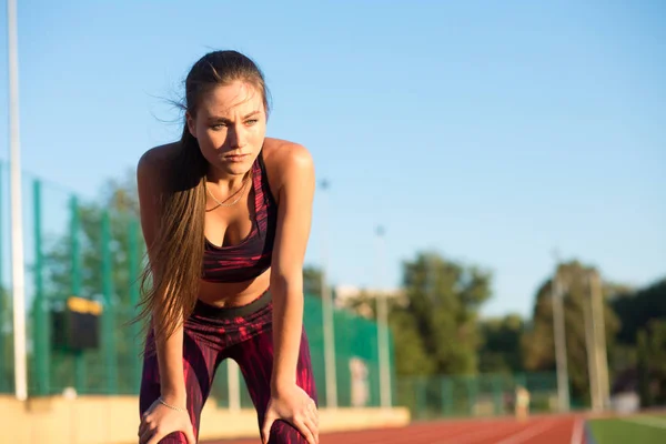 Mujer joven de pie inclinada y recobrando el aliento durante una sesión de carrera — Foto de Stock