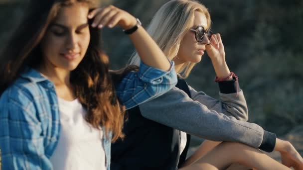 Duas jovens viajantes. Estilo de moda de meninas sentadas e usando óculos de sol ao pôr do sol . — Vídeo de Stock