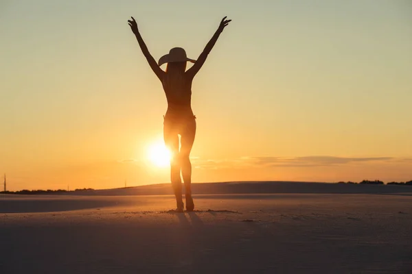 Silhouette of freedom woman with raised hands in gold desert at sunset