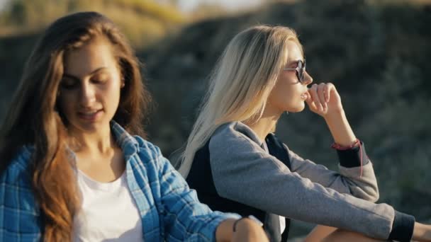 Deux jeunes voyageuses. Style de mode des filles assises et portant des lunettes de soleil au coucher du soleil . — Video