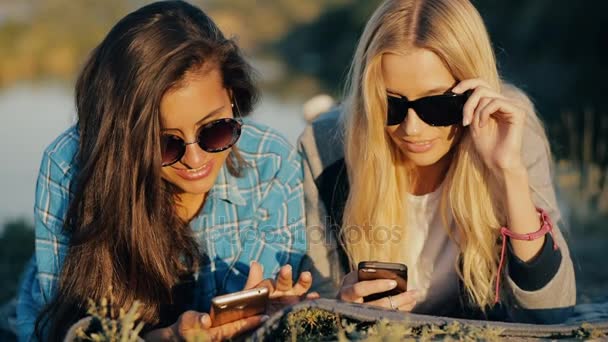Twee jonge reiziger vrouwen. Beste vrienden, liggend op een grond en neerkijken op slimme telefoons. — Stockvideo