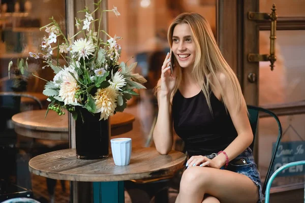 Arkadaşıyla ile akıllı telefonla konuşurken açık kafede oturan kadın — Stok fotoğraf