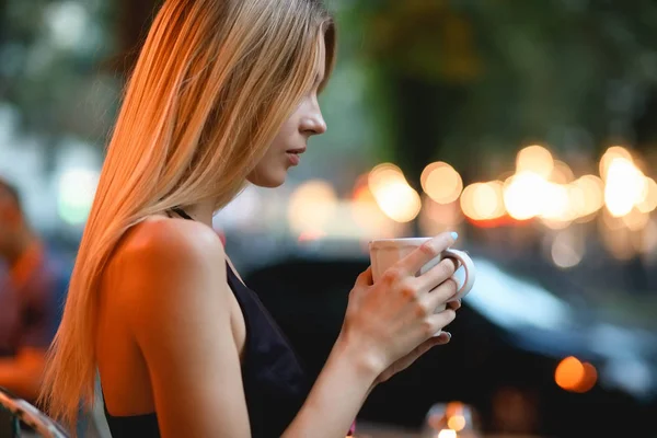 Vrouw zitten in een cafe drinken heerlijke latte. Koffiepauze openlucht in avond. — Stockfoto