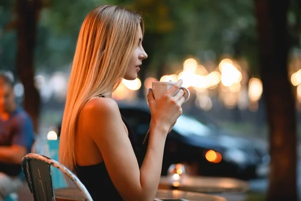 ผู้หญิงนั่งอยู่ในคาเฟ่ ดื่มลาเต้อร่อย กาแฟพักกลางแจ้งตอนเย็น . — ภาพถ่ายสต็อก