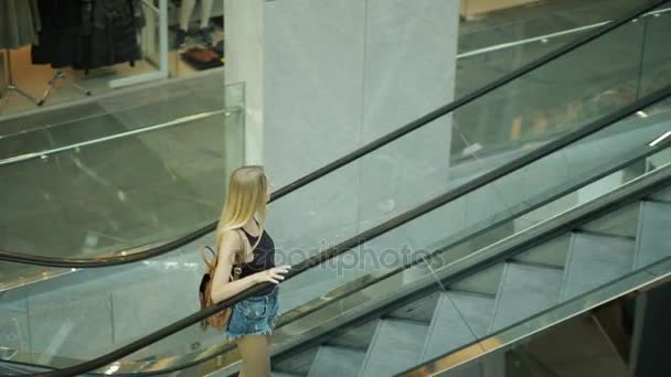Mujer en un centro comercial va por escaleras mecánicas, escaleras de transporte, escaleras móviles — Vídeos de Stock