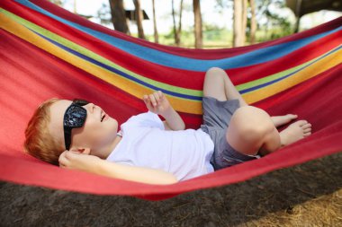 Bir çam ormanı, doğa dinlenme ve gökyüzüne bakarak o hamakta yatan güneş gözlüğü ile neşeli küçük çocuk
