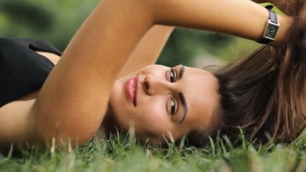 Donna attraente sdraiata sull'erba durante l'estate, si rilassa e gioca civettuola con i capelli . — Video Stock
