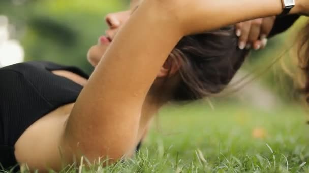 Приваблива жінка лежить на траві в літній час, вона розслабляється і кокетливо грає з волоссям . — стокове відео