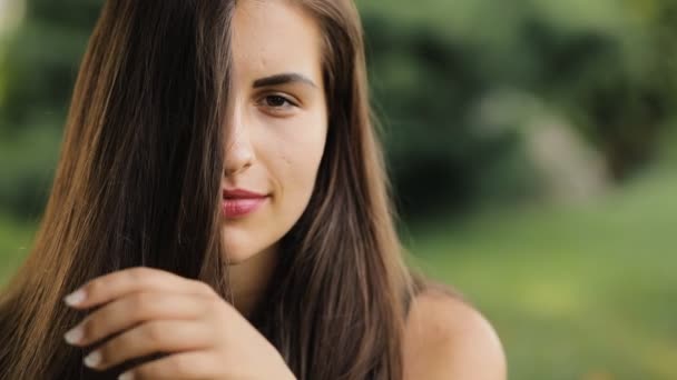 Retrato de cerca de una mujer bonita con cabello hermoso en un parque en el día de verano — Vídeos de Stock