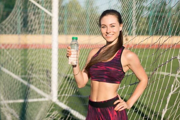 年轻快乐的女人的肖像放瓶水。微笑在喝坚持体育场户外运动装的女运动员。健康的生活方式的概念. — 图库照片