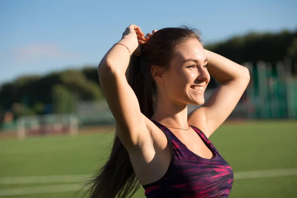 Joven deportista feliz en ropa deportiva atar el pelo cola de caballo en el estadio al aire libre . — Foto de Stock