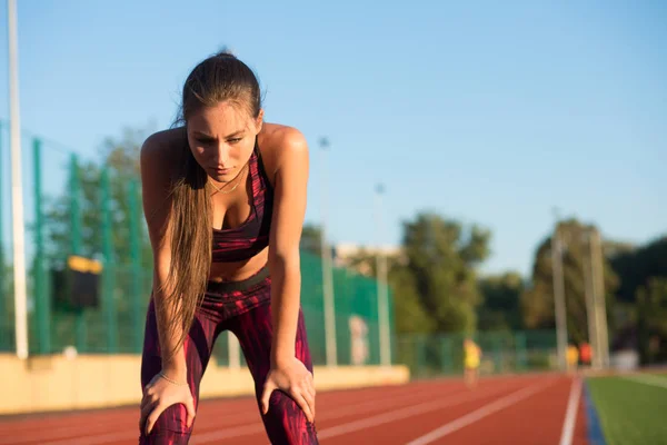 Mujer joven de pie inclinada y recobrando el aliento durante una sesión de carrera — Foto de Stock