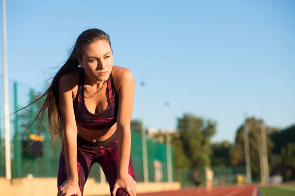 Young woman standing bent over and catching her breath during a running session — Stock Photo, Image