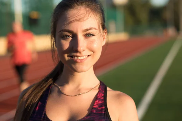 Bliska portret szczęśliwy młody uśmiechający się sportowy kobieta lekkoatleta sprinter w sportowej na torze stadionu na zewnątrz. Koncepcja zdrowy styl życia, aktywność sportowa. — Zdjęcie stockowe