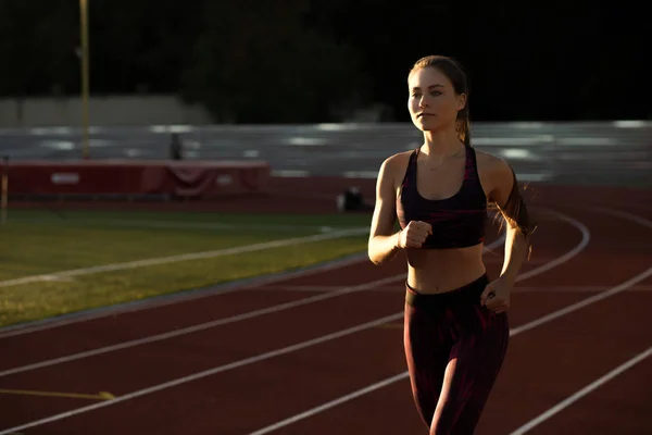 Deportista profesional corriendo al aire libre al atardecer. Atleta femenina en ropa deportiva en el estadio al aire libre. Actividad deportiva de entrenamiento . — Foto de Stock