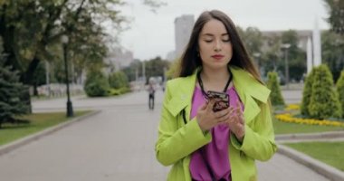 Mutlu kadın şehir sokakta bulutlu yaz veya sonbahar günü, steadicam atış yürüyüş smartphone tarafından konuşma