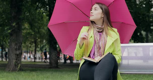 Vrouw zitten op bankje onder de paraplu en lezing boek op bewolkte zomer of herfst dag — Stockvideo