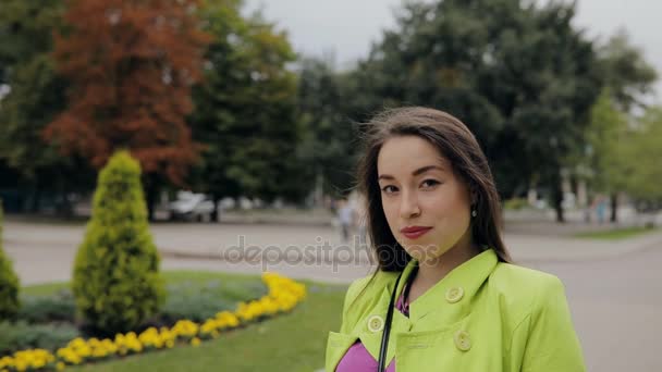 Mujer seria mira hacia abajo a la cámara de pie en otoño parque al aire libre — Vídeo de stock