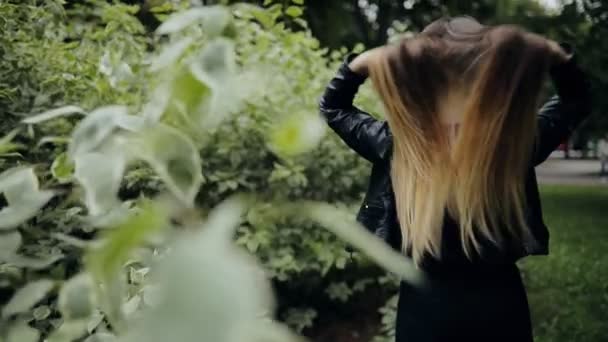 Mulher atraente em jaqueta preta jogando cabelo no parque de verão, câmera lenta — Vídeo de Stock