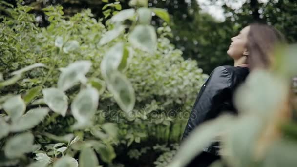 Привлекательная женщина в черной куртке бросает волосы в летнем парке, замедленная съемка — стоковое видео