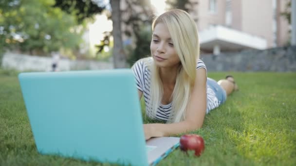 Mulher bonita blogger ou freelancer trabalhando com seu laptop ao ar livre deitado na grama no parque — Vídeo de Stock