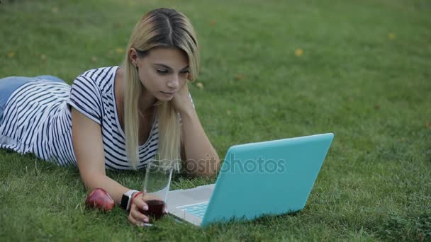 Mujer bonita blogger o freelancer trabajando con su portátil al aire libre tumbado en la hierba en el parque — Vídeo de stock