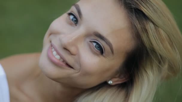 Mulher bonita retrato, close-up sorridente rosto em câmera lenta, menina atraente com cabelo bonito sentado na grama — Vídeo de Stock