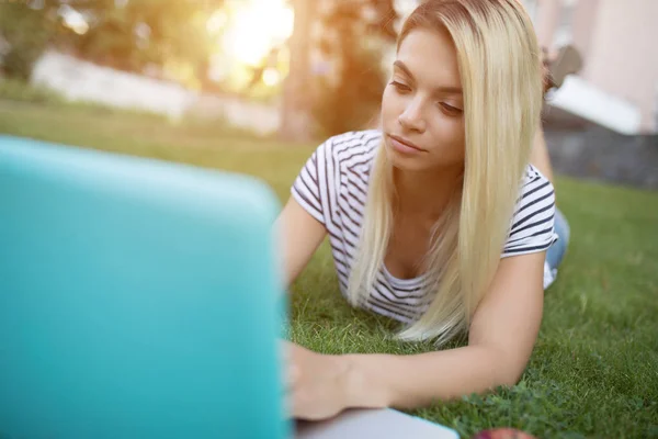 Mulher bonita blogger trabalhando com seu laptop ao ar livre deitado na grama no parque — Fotografia de Stock