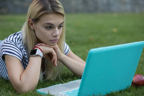 Mulher bonita blogger tristemente olhando para o seu laptop ao ar livre deitado na grama no parque — Fotografia de Stock