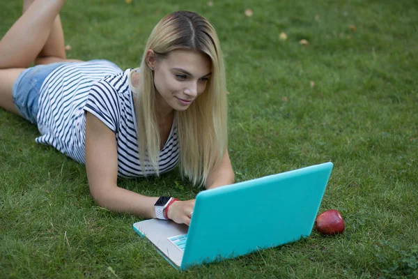 Mulher bonita blogger trabalhando com seu laptop ao ar livre deitado na grama no parque — Fotografia de Stock