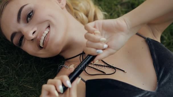 Hermosa mujer acostada en una hierba, chica haciendo maquillaje y sonrisa en cámara lenta, atractivos colores femeninos los labios — Vídeos de Stock