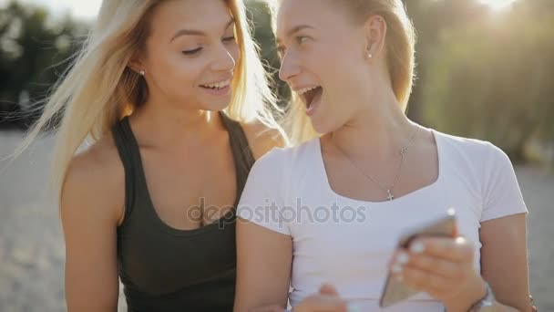 Filles amis qui cherchent à smartphone dans une plage pendant les vacances d'été, au ralenti — Video