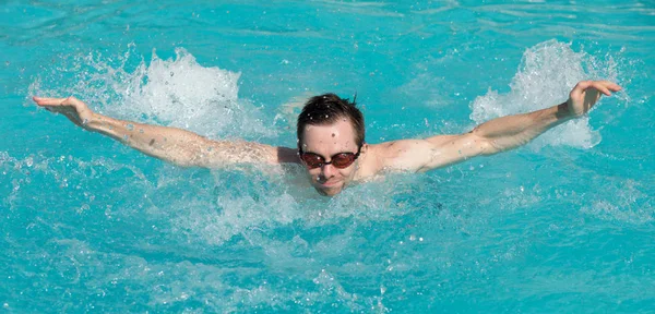 Joven con gafas de agua nadar en una piscina, estilo mariposa — Foto de Stock