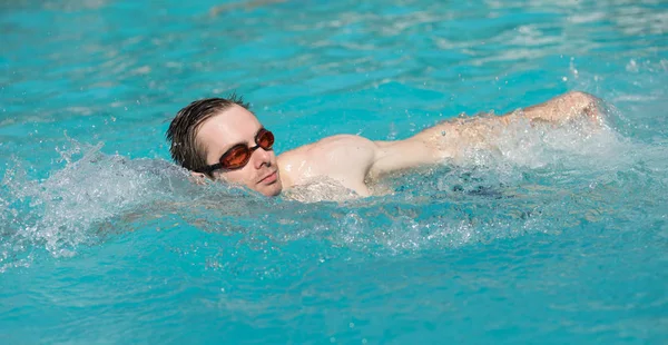 Ung man med vatten skyddsglasögon bada i en pool, crawl stil — Stockfoto