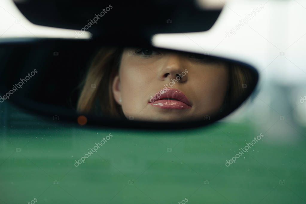 Beautiful woman looking to her face in rearview mirror of her car