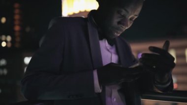 Gece şehir ayakta balkon akıllı telefon isteyen genç Afrika işadamı
