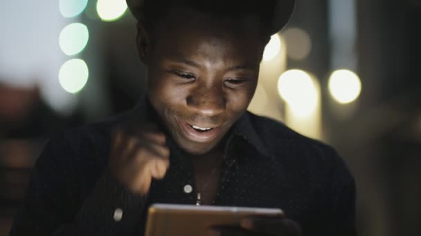 Νεαρός αφρικανική ψάχνει που εκπέμπουν online Ποδοσφαιρικό αγώνα στο smartphone στην πόλη τη νύχτα — Αρχείο Βίντεο