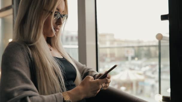 Kobieta w kawiarni przy użyciu smartfona, ona patrzy na telefon — Wideo stockowe