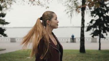 Sonbahar geliyor. Mutlu kadın bordo deri ceketli yürüyerek şehir sokak, slowmotion.