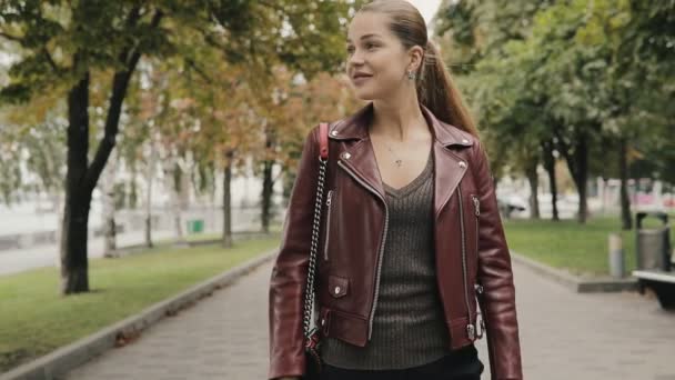 Llega el otoño. Mujer en chaqueta de cuero color burdeos caminar en la calle de la ciudad, slow motion . — Vídeos de Stock