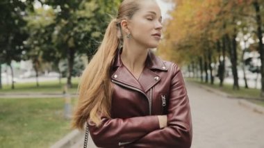 Sonbahar geliyor. Bordo deri ceket kadında yürüyerek şehir sokak, slowmotion.